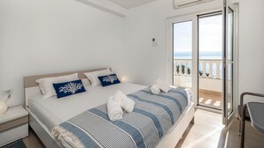 Une chambre à coucher comprenant un lit, des oreillers, une table de chevet, un appareil de climatisation et un balcon avec vue.