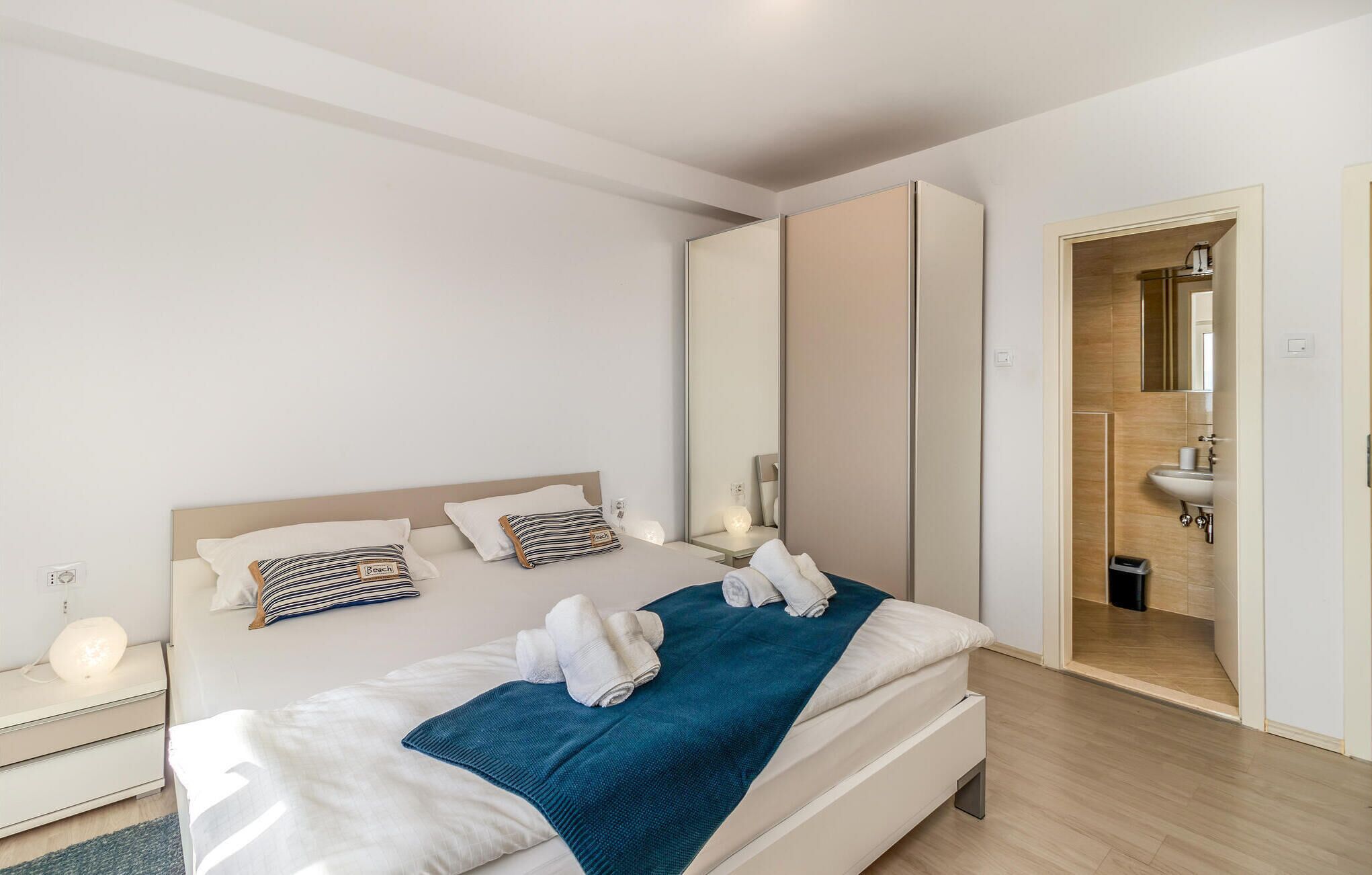 A modern hotel room with a large bed, a bedside table, a mirror, and a bathroom visible through an open door.