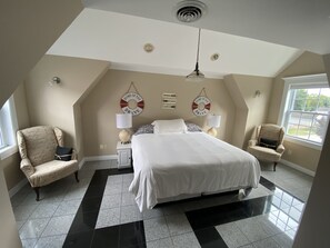 Ein Schlafzimmer mit einem großen Bett, zwei Stühlen, einem Nachttisch und einem Deckenventilator.