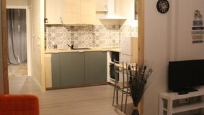A modern kitchen with patterned backsplash, a dining area with chairs, a TV on a stand, and a decorative vase. - Maison a 2 pas des Volcans (Lanobre)