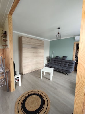 A spacious living room with a large wooden wardrobe, a grey sofa, a white coffee table, and a wooden floor. - Maison a 2 pas des Volcans (Lanobre)