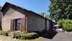 A stone building with a sloped roof, a wooden door, and a small patio with outdoor furniture. - Maison a 2 pas des Volcans (Lanobre)