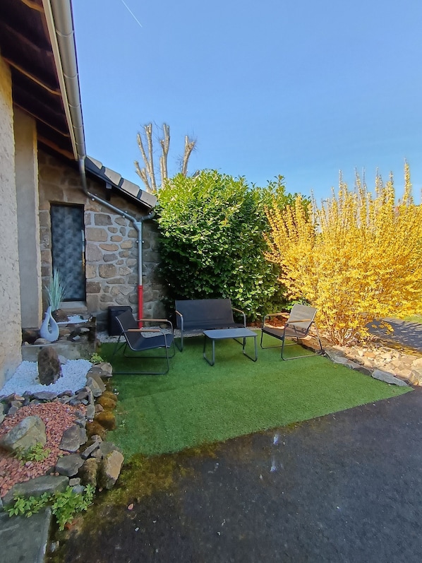 A patio with outdoor furniture, a stone wall, and a well-maintained lawn. - Maison a 2 pas des Volcans (Lanobre)