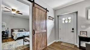 Una habitación con puerta corredera estilo granero, una cama con colcha estampada, un escritorio con silla y un ventilador de techo.