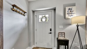 Un pasillo con una puerta blanca, un perchero, un cartel de bienvenida, una lámpara y un enchufe.
