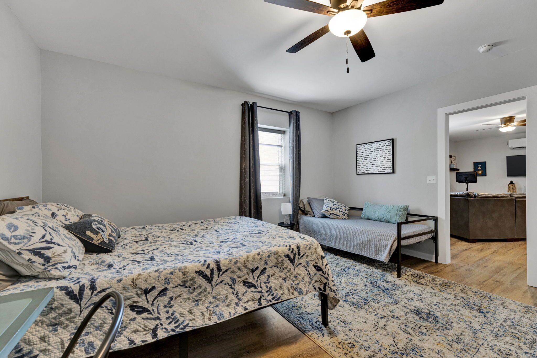 Un dormitorio con cama, escritorio, silla, ventilador de techo y ventana con cortinas.
