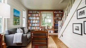A cozy living room with a grey sofa, wooden bookshelves, and a staircase.