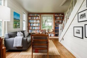 Una sala de estar acogedora con un sofá gris, estanterías de madera y una escalera.