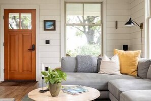 Un salón con sofá gris, puerta de madera y ventana con vistas a zonas verdes.