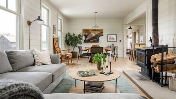 A cozy living room with a sofa, coffee table, and fireplace. There is a dining area with chairs and a table, and a painting on the wall.
