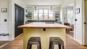 A spacious kitchen with a central island, two stools, and a large window providing natural light.