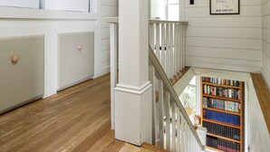 A laundry room with stacked washers and dryers, a staircase leading to a lower level, and a bookshelf with books.