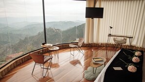 A spacious room with a large window offering a mountain view, a bed with a black bedspread and flowers, a TV, and a small table with a chair. - Atardeceres del cafe (Manizales)
