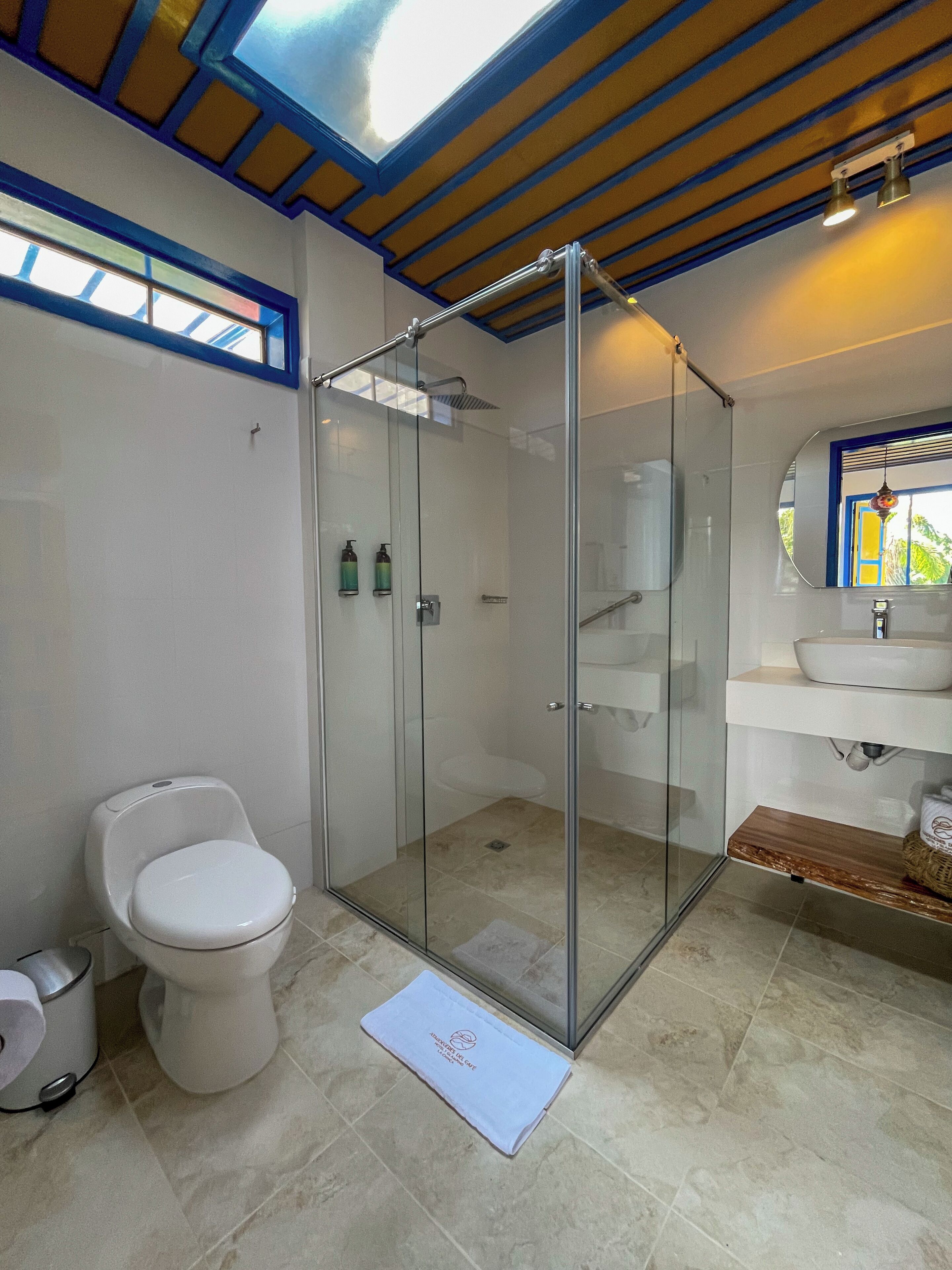 A modern bathroom with a glass-enclosed shower, a toilet, and a sink with a wooden shelf.