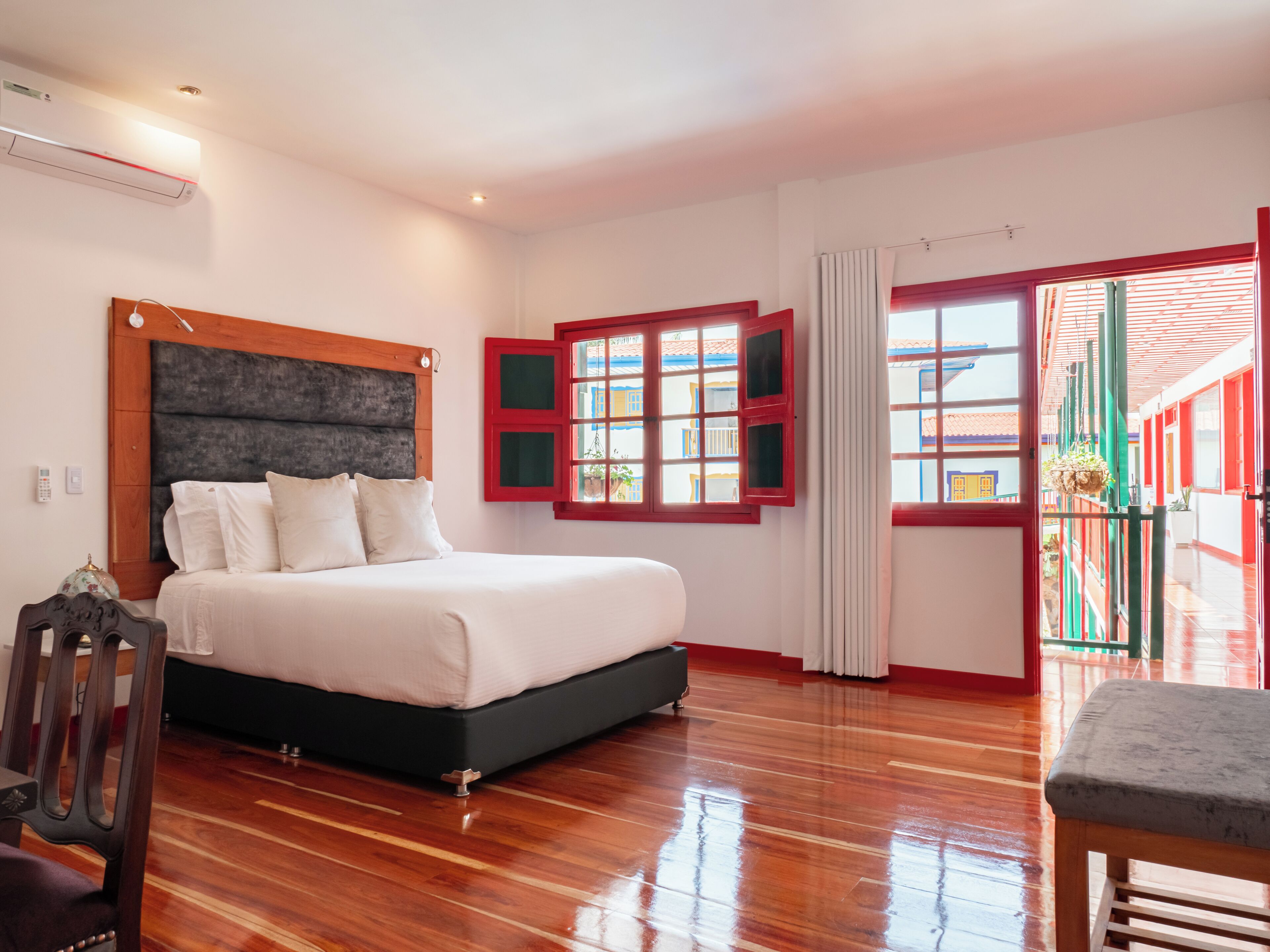 Quarto com uma cama grande, piso de madeira e vista pela janela com persianas vermelhas.