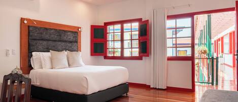 Quarto com uma cama grande, piso de madeira e vista pela janela com persianas vermelhas.