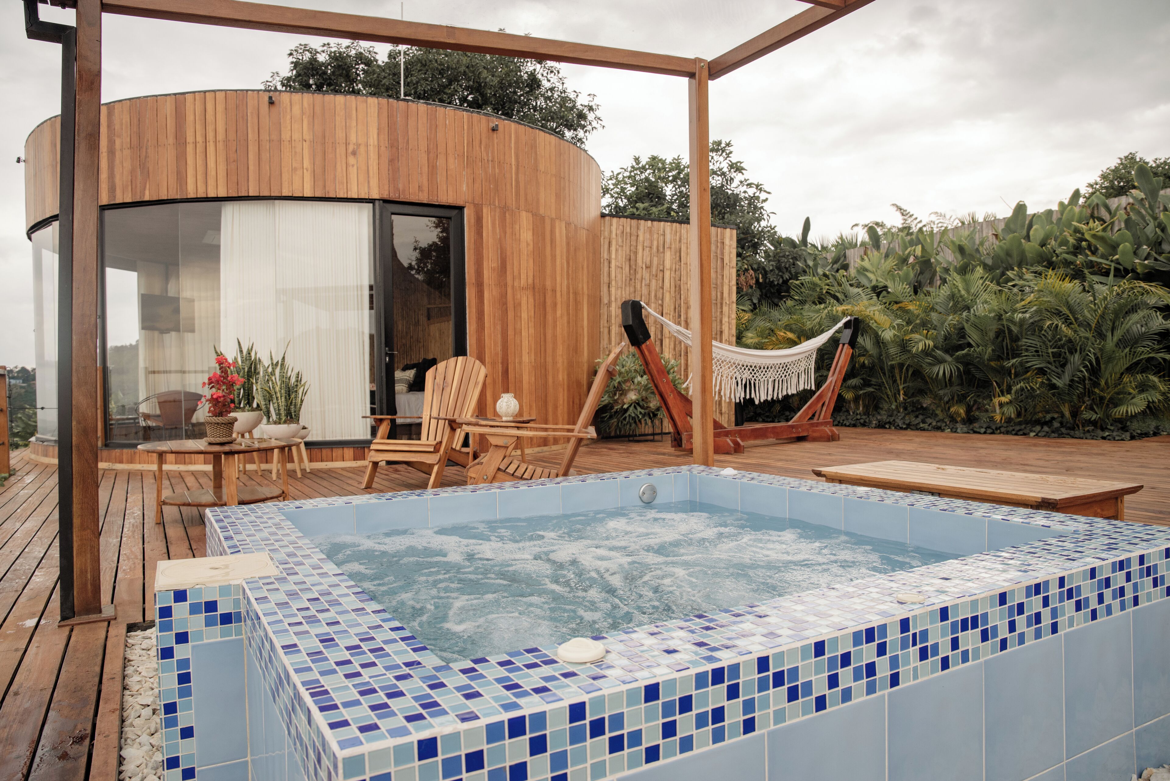 Ein moderner Außenbereich mit Whirlpool, Holzterrasse, Liegestühlen und einer Hängematte.
