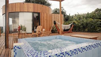 Ein moderner Außenbereich mit Whirlpool, Holzterrasse, Liegestühlen und einer Hängematte.