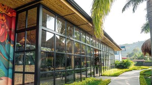A modern building with large glass windows, a wooden ceiling, and a pathway lined with greenery. - Atardeceres del cafe (Manizales)