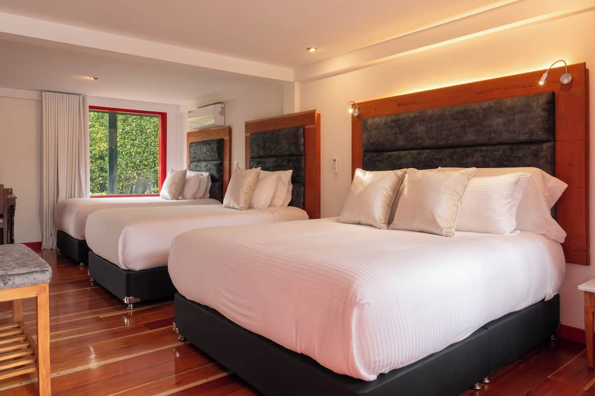 A modern hotel room with two beds, wooden flooring, and a large window with a view of greenery.