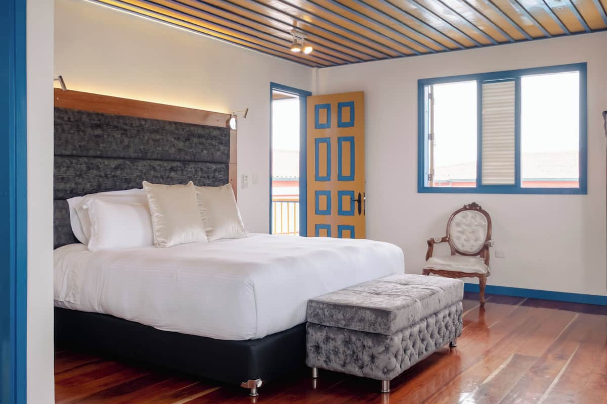 A bedroom with a wooden ceiling, a bed, a nightstand, a chair, and a window.