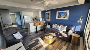 A modern living room with a grey sofa, a coffee table, and a kitchen in the background. - Beautiful updated oceanfront 1 bedroom 1 bath, full kitchen, direct oceanfront  (Daytona Beach)
