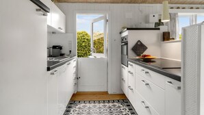 A modern kitchen with white cabinets, a black countertop, and a patterned rug. - Cozy home in Idestrup with WiFi (Idestrup)