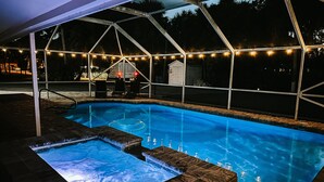 Una piscina con un jacuzzi, rodeada por una zona techada con guirnaldas de luces.