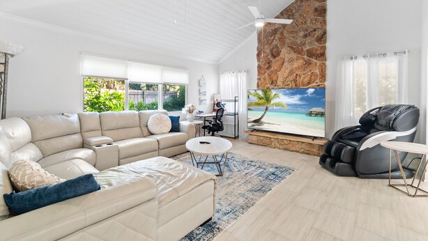 Un salón amplio con un sofá grande, un sillón de masaje, una mesita redonda y una pared de piedra decorativa.