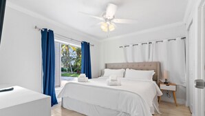 Un dormitorio moderno con una cama grande, una mesita de noche, un ventilador de techo y vistas al exterior.