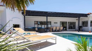 A poolside area with lounge chairs, a pergola, and a modern building with large windows.