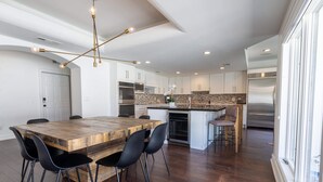 A modern kitchen with a wooden island, black chairs, and stainless steel appliances.