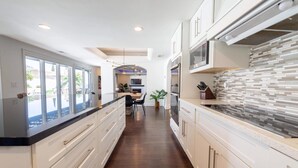 A modern kitchen with white cabinetry, a black countertop, and a tiled backsplash.