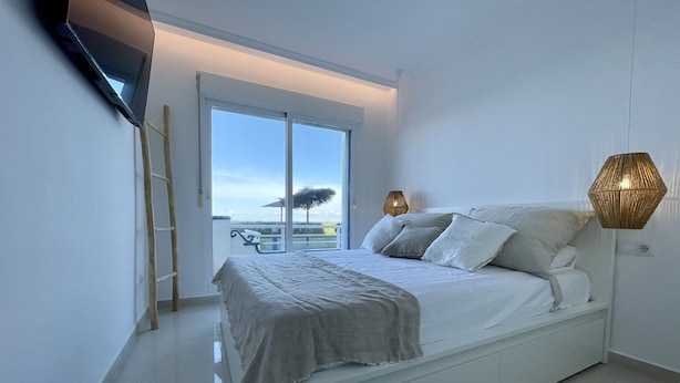Une chambre moderne avec un lit, une télévision, un balcon offrant une vue et une lampe.