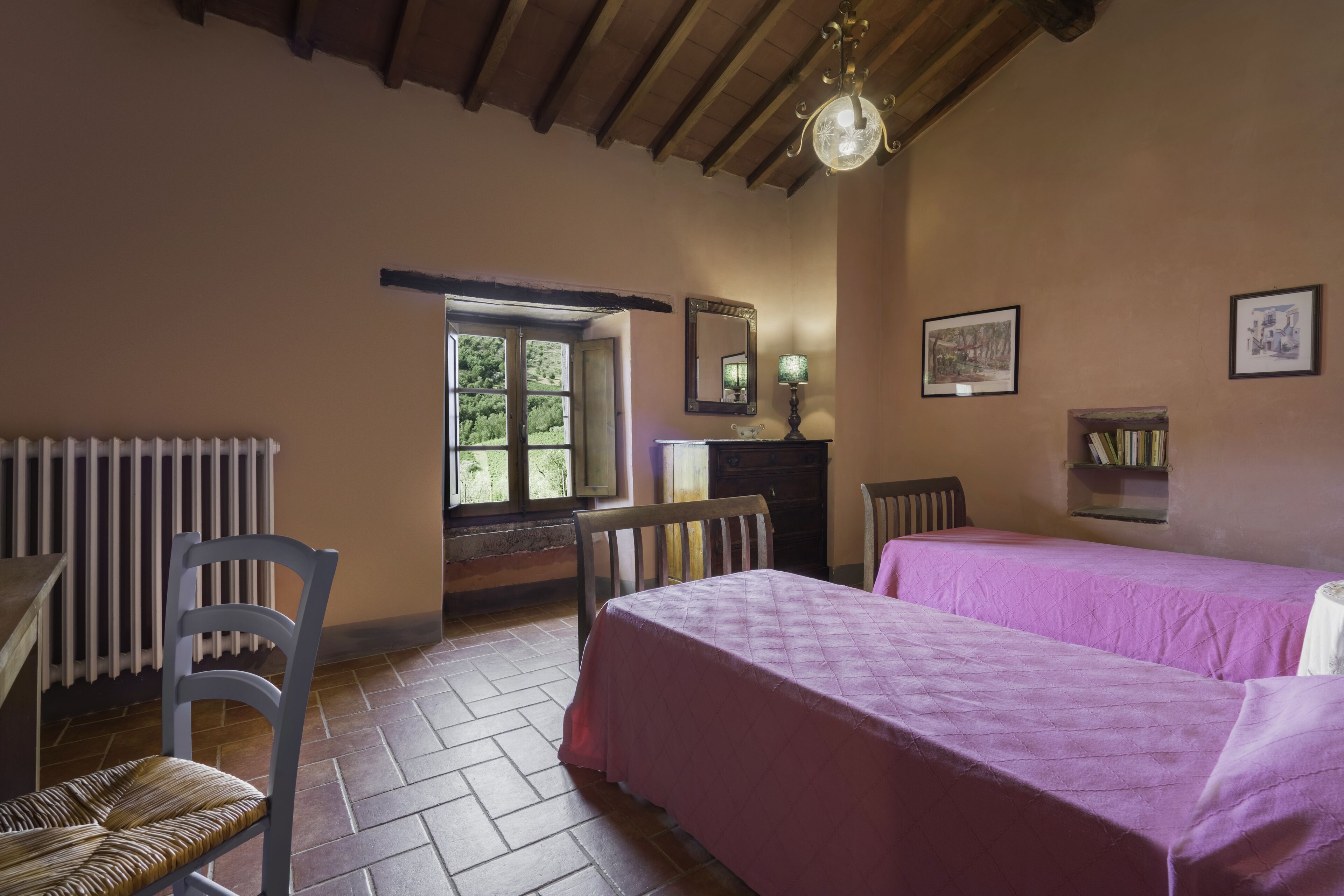 Een kamer met een bed, een stoel, een tafel, een radiator, een raam en een spiegel.
