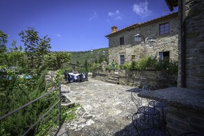 Un edificio de piedra con un patio, mobiliario exterior y vistas a la vegetación circundante.