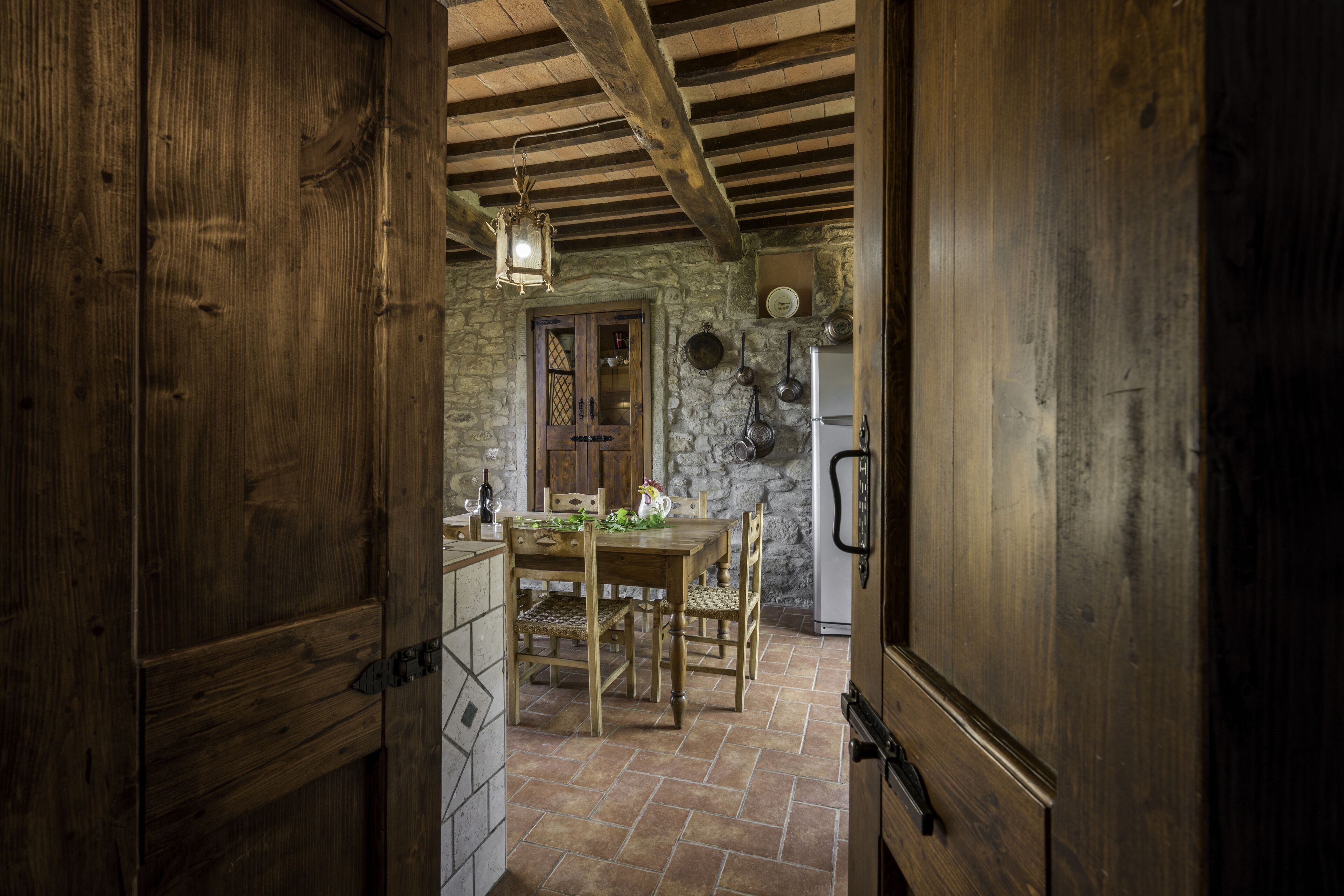 A rustic kitchen with a stone wall, wooden ceiling beams, and a tiled floor.