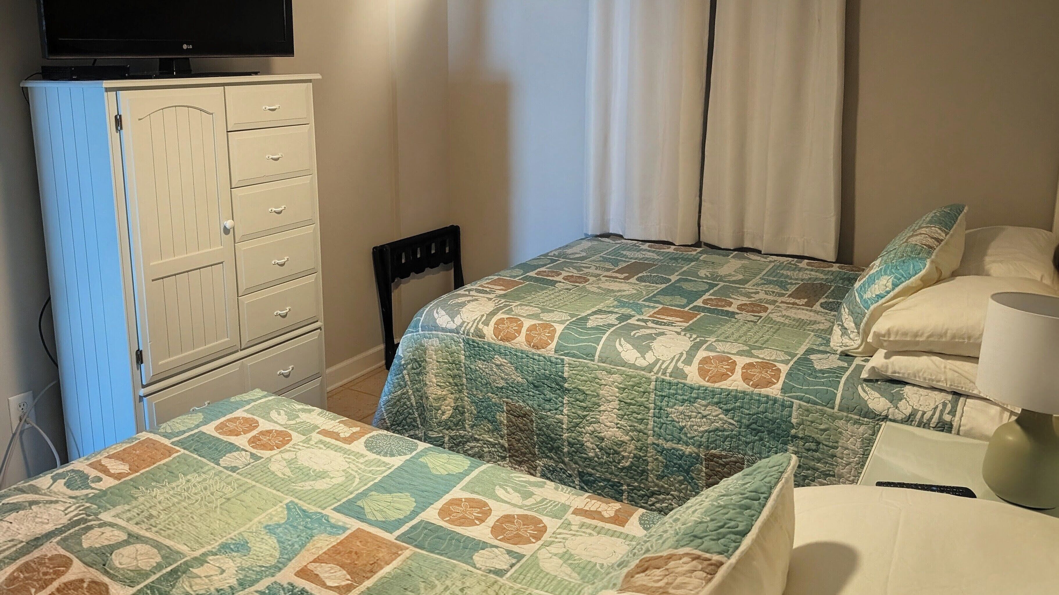A bedroom with two beds, a dresser, and a television.
