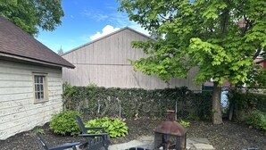 Un jardin avec une terrasse en pierre, quatre chaises Adirondack, un foyer en métal et une clôture en bois.