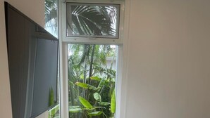 A modern, well-lit room with a large window, a flat-screen TV, a white desk, and a bed. - Private Garden Condo - 5 min from the Beach (Koh Samui)