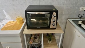 A kitchen with a black toaster oven on a wooden shelf, a yellow basket, and a white countertop. - S320 - Sirolo, one bedroom apartment with breathtaking view (La Madonnina)