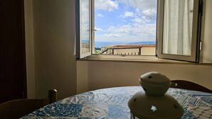 A room with a window overlooking a balcony, a table with a patterned tablecloth, and a white object on the table. - S320 - Sirolo, one bedroom apartment with breathtaking view (La Madonnina)