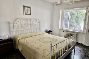 A room with a bed, a window, a radiator, and a framed picture on the wall.