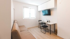 Un espace de vie compact comprenant un canapé, une table à manger avec des chaises, un téléviseur fixé au-dessus de la table et une fenêtre laissant entrer la lumière naturelle.
