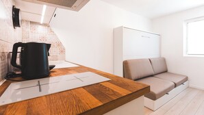 Une cuisine moderne avec un plan de travail en bois, une bouilloire et un tableau blanc. La pièce est également équipée d’un canapé beige et d’une armoire blanche.