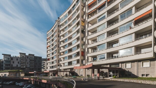 Un immeuble résidentiel à plusieurs étages, doté de balcons, d’une entrée abritée et d’un espace de stationnement.