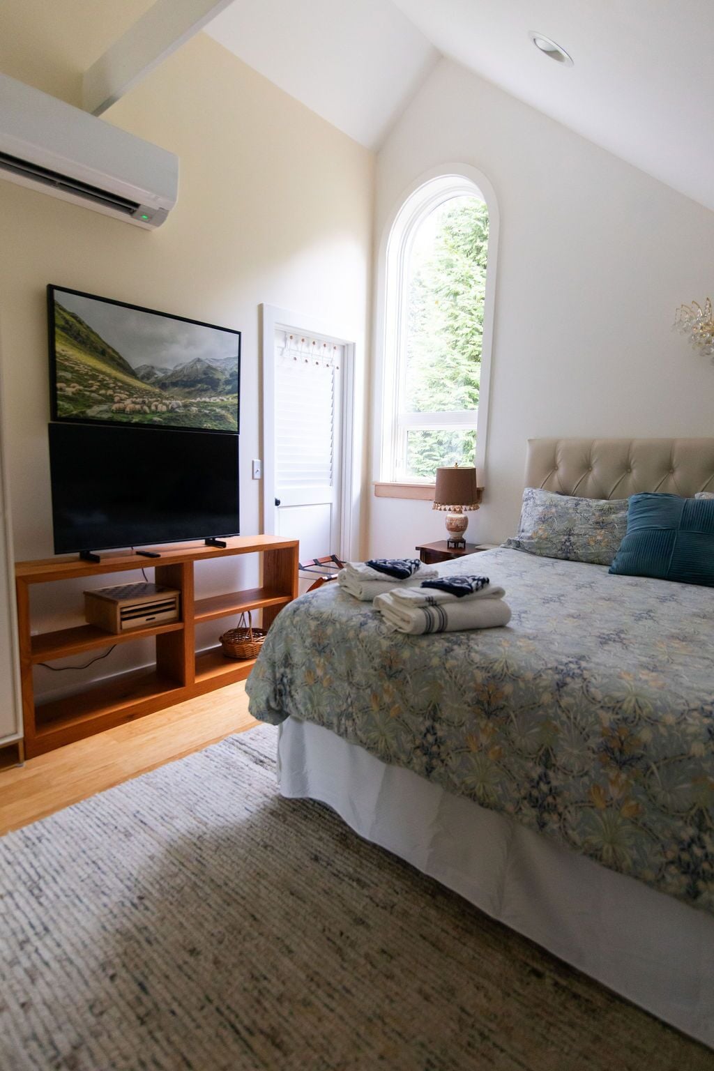 Une chambre dotée d’un grand lit, d’un téléviseur à écran plat, d’une fenêtre donnant sur un paysage verdoyant et d’un meuble TV en bois.