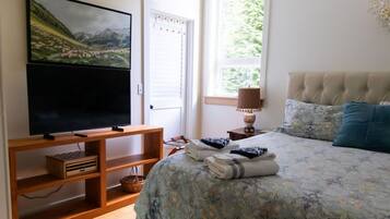 Une chambre dotée d’un grand lit, d’un téléviseur à écran plat, d’une fenêtre donnant sur un paysage verdoyant et d’un meuble TV en bois.