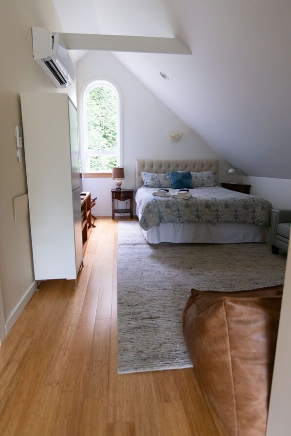 A bedroom with a large bed, a window, a ceiling fan, and a wooden floor.