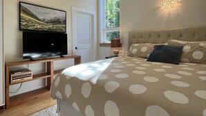 Een slaapkamer met een groot bed, een televisie, een raam en een plafondlamp.